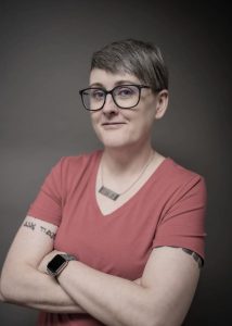 Dr Liz Rodwell, wearing a red shirt and glasses with short grey hair